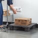 A woman stacking a cardboard box on a Lavex Modular black pallet base.