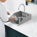 A person washing dishes in a Waterloo stainless steel drop-in sink with a gooseneck faucet.