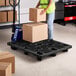 A woman holding a box standing on a black plastic pallet.