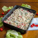 A black Carlisle rectangular deli crock filled with pasta and tomatoes on a table.