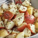 A bowl of potato wedges seasoned with Regal Brown Mustard Seed with green and red specks and green onions.