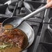 A Tablecraft stainless steel spoon with black silicone head pouring sauce on a meat dish.