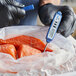 A blue digital pocket probe thermometer being used to measure the temperature of raw fish.
