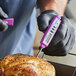 A purple digital pocket probe thermometer being used to check the temperature of cooked poultry.