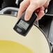 A person using a CDN Mini Digital Infrared Thermometer to measure the temperature of food in a pan on a kitchen counter.