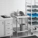 A Regency stainless steel filler table with a drop-in sink and faucet over a sink with shelves.