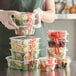 A woman in a green apron holding Choice clear plastic containers filled with food.