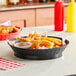 A black Tablecraft diner platter basket filled with fried food on a table.