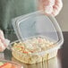 A person in gloves holding a Choice clear plastic deli container filled with food.