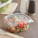 A clear Choice plastic deli container filled with salad with a fork and knife on the side.