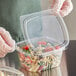 A gloved hand holds a clear Choice RPET deli container full of food.