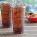 Two Choice clear plastic cups filled with ice tea on a table.