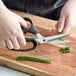 A person using Mercer Culinary kitchen shears to cut chives on a cutting board.