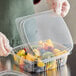 A person in gloves holding a Choice clear plastic deli container of fruit.