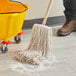 A person using a Choice Natural Cotton Cut End Wet Mop to clean the floor in a yellow bucket on wheels.