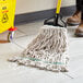 A person using a Choice Natural Cotton Looped End Wet Mop to clean a floor in a room with a yellow caution sign.