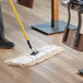 A person using a Choice Natural Cotton Cut-End Dry Dust Mop Head to clean a floor.