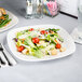 A Tuxton white square china plate with a salad and a glass of water on it.