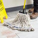 A person cleaning a floor with a Choice Natural Cotton Looped End Wet Mop Head.