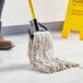 A person cleaning a floor with a Lavex Natural Cotton Wet Mop.