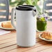 A white Tablecraft plastic pitcher with a black lid on a table with food.