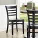 A Lancaster Table & Seating black wood ladder back chair with black wood seat on a table in a restaurant dining area.