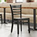 A Lancaster Table & Seating black wood ladder back chair with a black wood seat next to a table in a restaurant.