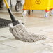 A Lavex natural cotton wet mop head with a yellow headband on a wood floor.