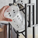 A hand holding a white Tablecraft polypropylene container with holes filled with spoons.