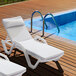 Two Lancaster Table & Seating white chaise lounges next to a pool.