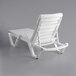 A white Lancaster Table & Seating resin chaise with a white cushion and pillow on a white background.