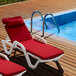 Two white Lancaster Table & Seating chaise loungers with red cushions next to a pool.