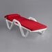 A white Lancaster Table & Seating chaise lounge with red cushions and pillow.