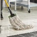 A person using a Lavex natural cotton wet mop with a yellow handle to clean a floor.