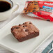 A gluten-free David's Cookies chocolate chip brownie on a white plate next to a cup of coffee.