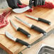 A Schraf boning knife with a black handle being used to cut raw meat on a cutting board.