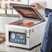 A person using a VacPak-It chamber vacuum packing machine to seal meat on a counter.