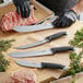 A person in black gloves using a Schraf butcher knife to cut meat on a counter.