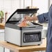 A chamber vacuum packing machine with a digital control panel and a 10-inch seal bar, shown in use sealing a bag of food.
