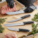 A person in black gloves using a Schraf Butcher Knife with a TPRgrip handle to cut meat.