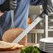 A man in a black shirt and gloves using a Schraf Smooth Edge Slicing Knife to cut meat on a counter.