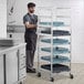 A man in a black apron standing next to a Regency aluminum glass rack cart.