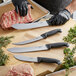 A person in black gloves using a Schraf Breaking Knife to cut meat on a counter.