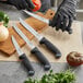 A person in black gloves uses a Schraf utility knife to cut a tomato on a cutting board.