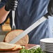 A person in a chef's uniform uses a Schraf slicing knife to cut meat.