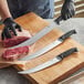 A person in gloves using a Schraf Cimeter knife to cut raw meat on a counter.