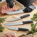 A person in black gloves using a Schraf Butcher Knife with a TPRgrip handle to cut meat on a counter.