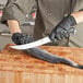 A person in black gloves using a Schraf Breaking Knife to cut a fish on a cutting board.