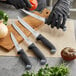 A person in black gloves using a Schraf serrated utility knife to cut a tomato.