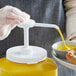 A person using a Tablecraft condiment pump to pour yellow liquid onto a plate of food.